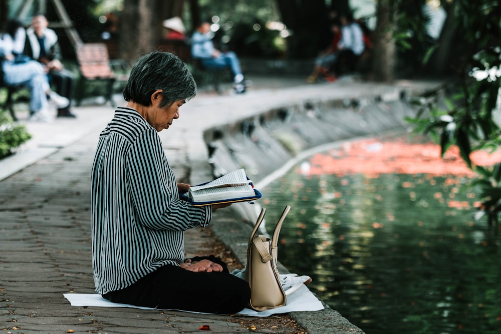 woman reading book near body of water
