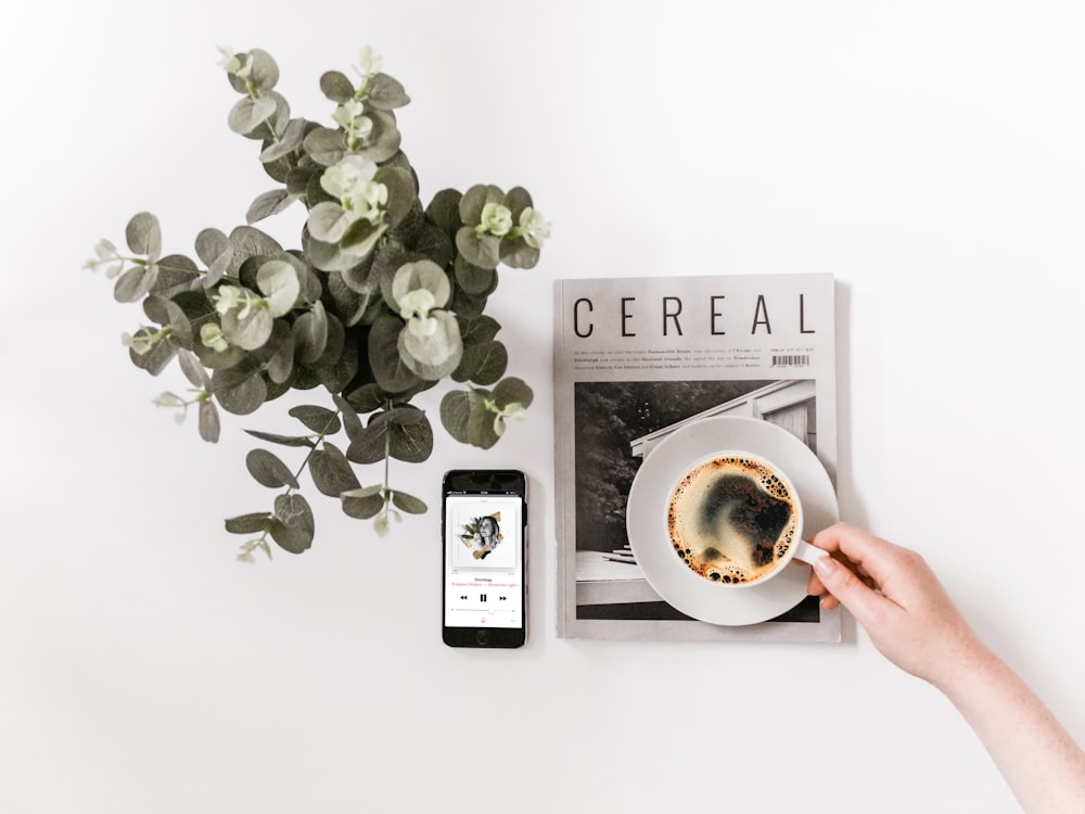 Fotografia plana de smartphone, jornal e xícara de chá