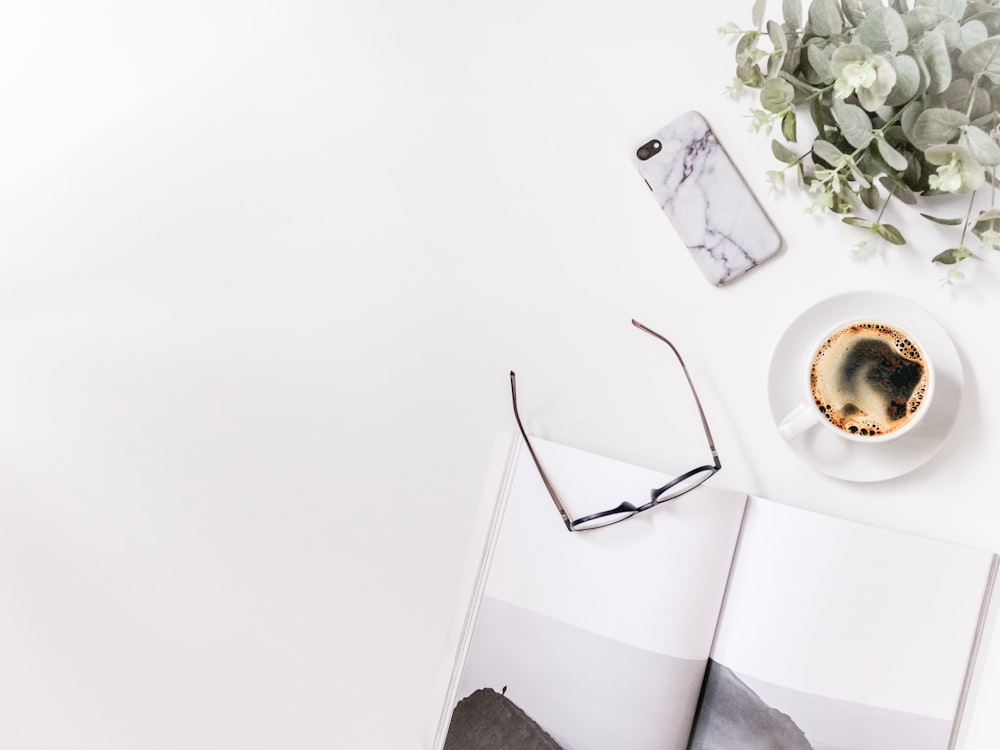 Des lunettes transparentes à côté d’une tasse à café blanche