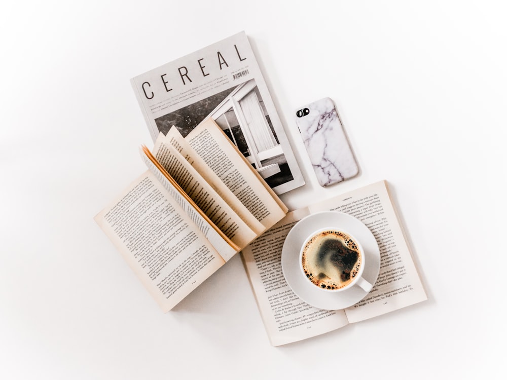 Tasse en céramique blanche avec du café sur soucoupe à côté des livres ouverts