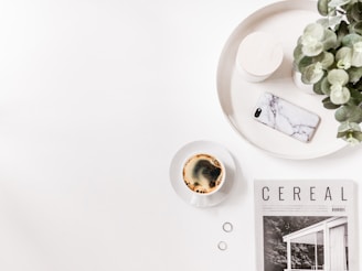 A vibrant flat lay of lifestyle magazines, plants, and a cup of coffee on a wooden table.