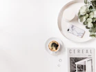 A vibrant flat lay of lifestyle magazines, plants, and a cup of coffee on a wooden table.