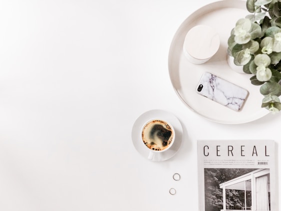 A vibrant flat lay of lifestyle magazines, plants, and a cup of coffee on a wooden table.