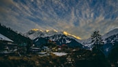 Snow-capped European mountains with a cozy village nestled below at dusk.