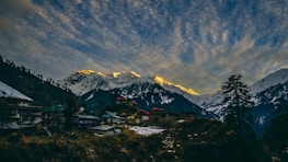 Snow-capped European mountains with a cozy village nestled below at dusk.