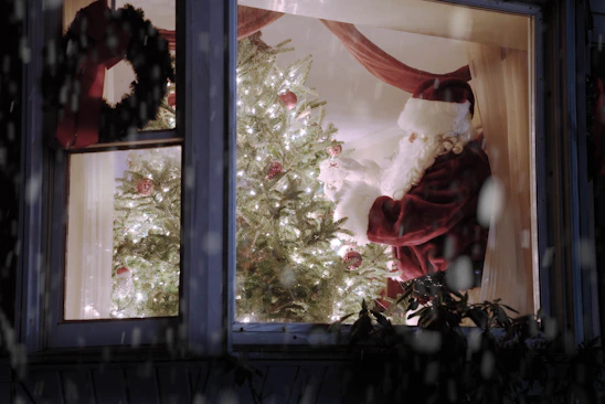 Santa Claus actor in a cozy North Pole-themed room, smiling warmly with twinkling Christmas lights and festive decorations.