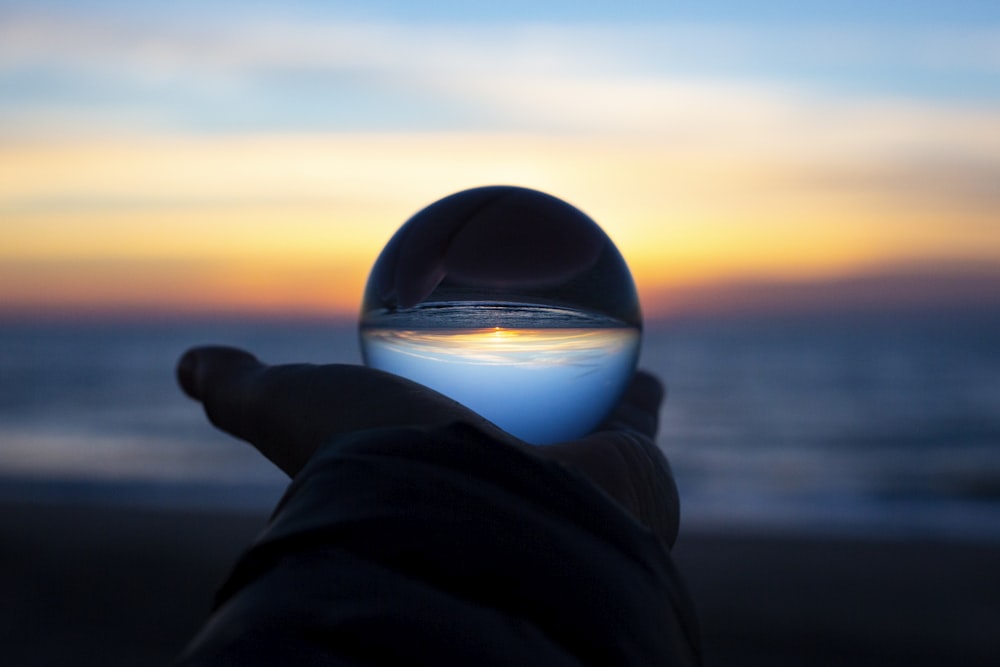 person holding clear glass ball at sunrise by Drew Beamer