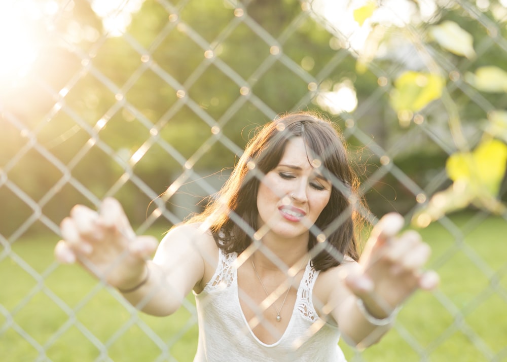 woman closing her eye while holding chain link fence outdoors