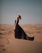 A model in a black lace dress standing against a desert sunset backdrop.