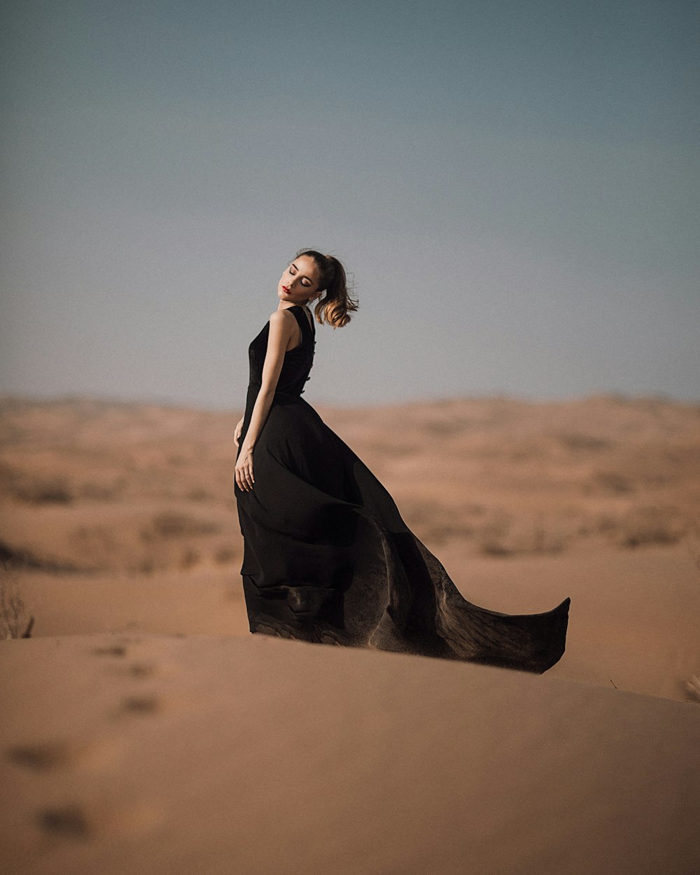 Frau im schwarzen Kleid steht in der Wüste