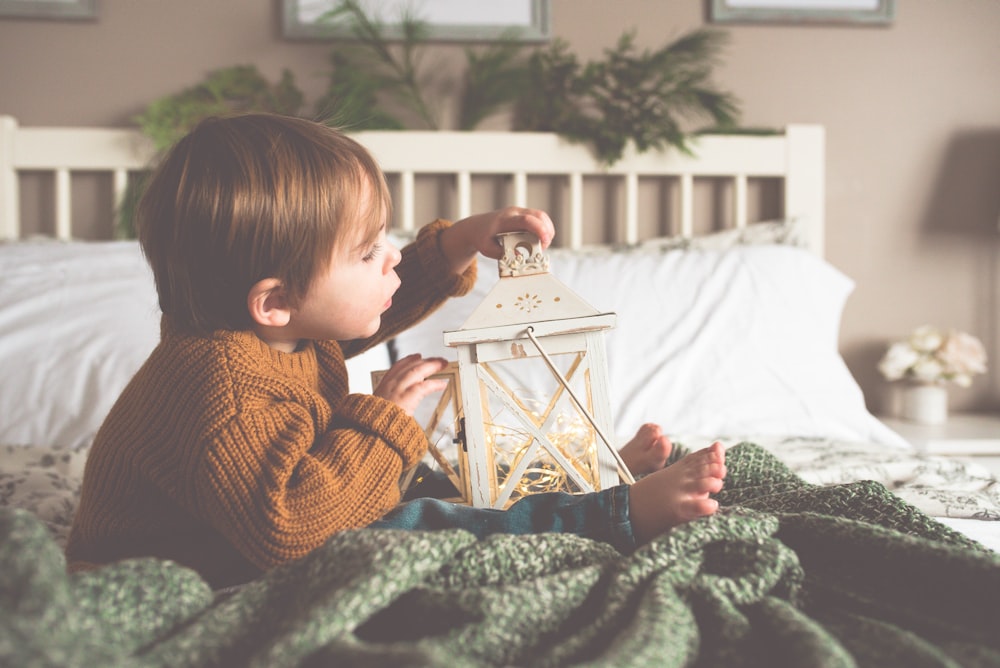 toddler holding candle lantern while sitting on bed