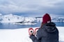 snowshoer sitting on snow overlooking calm ocean with icebergs under cloudy blue sky