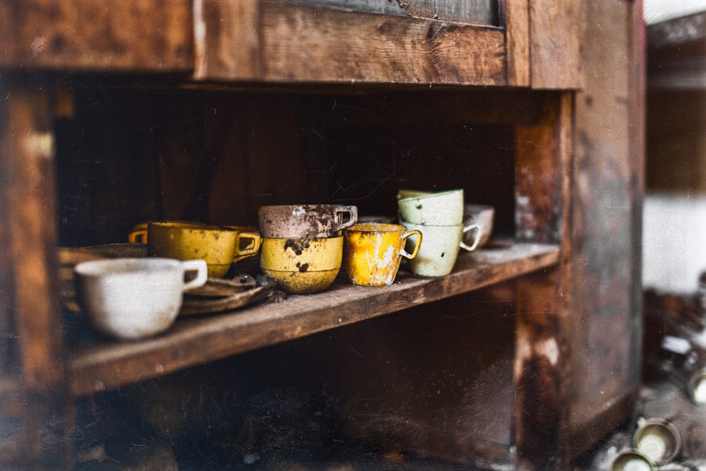 Farblich sortierte Teetassen auf braunem Holzregal