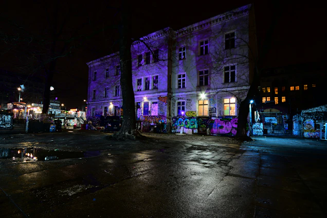 Dark urban street scene with graffiti and band posters glowing under neon yellow light.