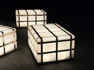 A series of glowing cube-shaped lamps with metal frames positioned on a dark tiled floor, creating a modern and minimalist aesthetic.