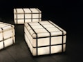 A series of glowing cube-shaped lamps with metal frames positioned on a dark tiled floor, creating a modern and minimalist aesthetic.