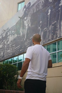A person wearing a sivam t-shirt standing proudly in front of a mural depicting historical impact figures.