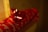 A close-up of a red gift box wrapped in red wrapping paper with white cursive writing. The box is adorned with a shiny red bow on top. The background is dimly lit, creating a warm and cozy atmosphere.