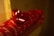 A close-up of a red gift box wrapped in red wrapping paper with white cursive writing. The box is adorned with a shiny red bow on top. The background is dimly lit, creating a warm and cozy atmosphere.