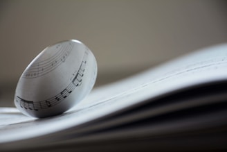 A glass orb sits on top of an open music sheet, distorting the musical notes through its lens-like surface. The focus is on the orb and the music notes visible through it, creating an artistic and abstract representation of music.