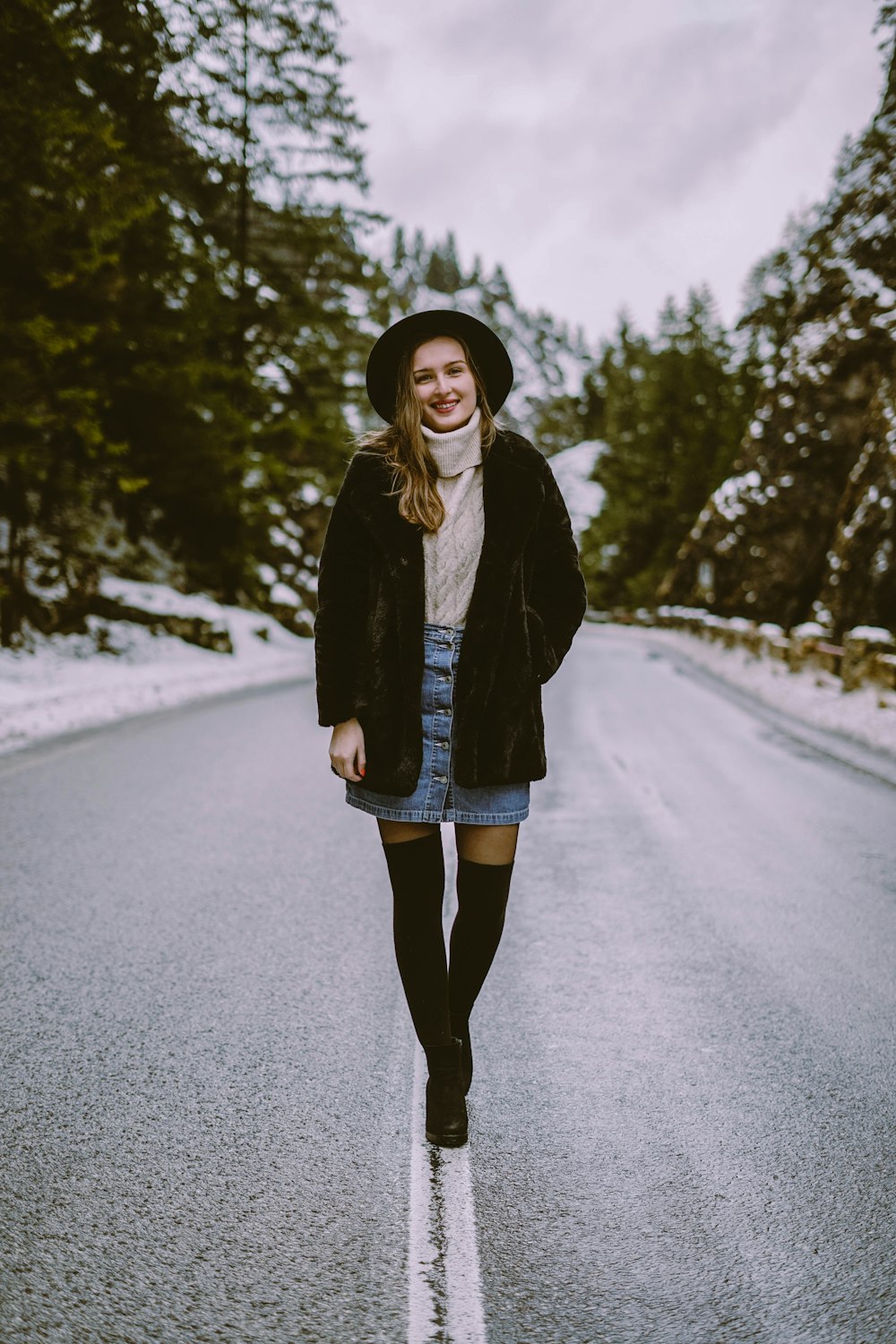 woman in black coat standing on road surrounded by trees during daytime