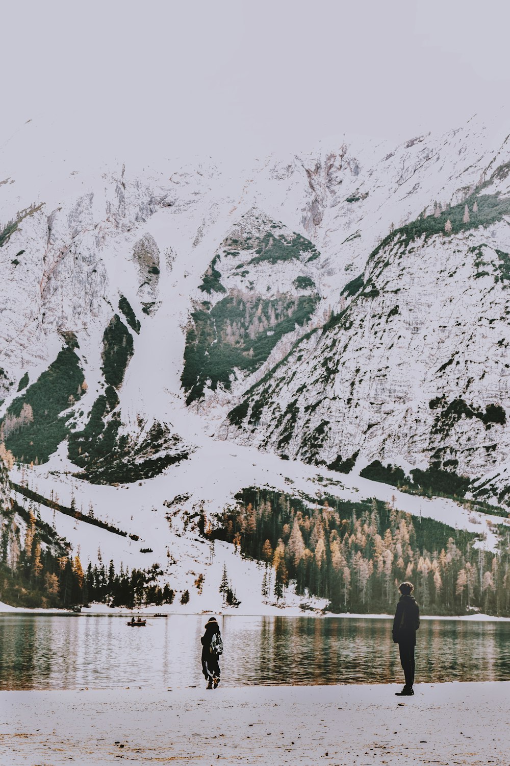 雪をかぶった山々に面した湖の前に立つ人