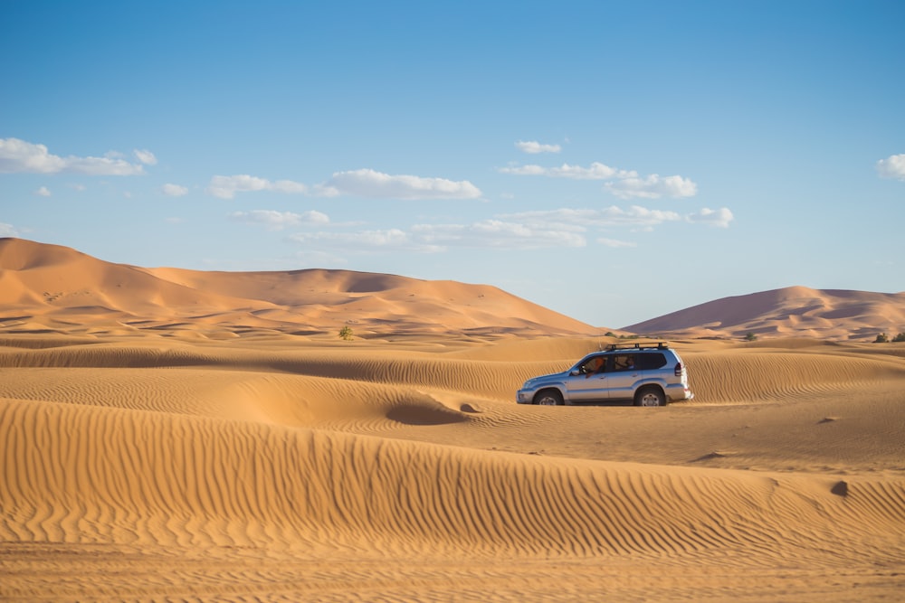 昼間の砂漠を走るシルバーのSUV