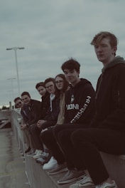 A diverse group of teenagers wearing trendy dark-themed outfits in an urban setting.