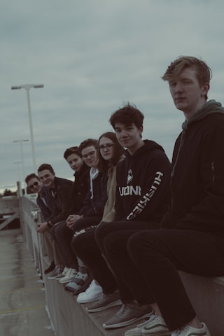 A diverse group of teenagers wearing trendy dark-themed outfits in an urban setting.