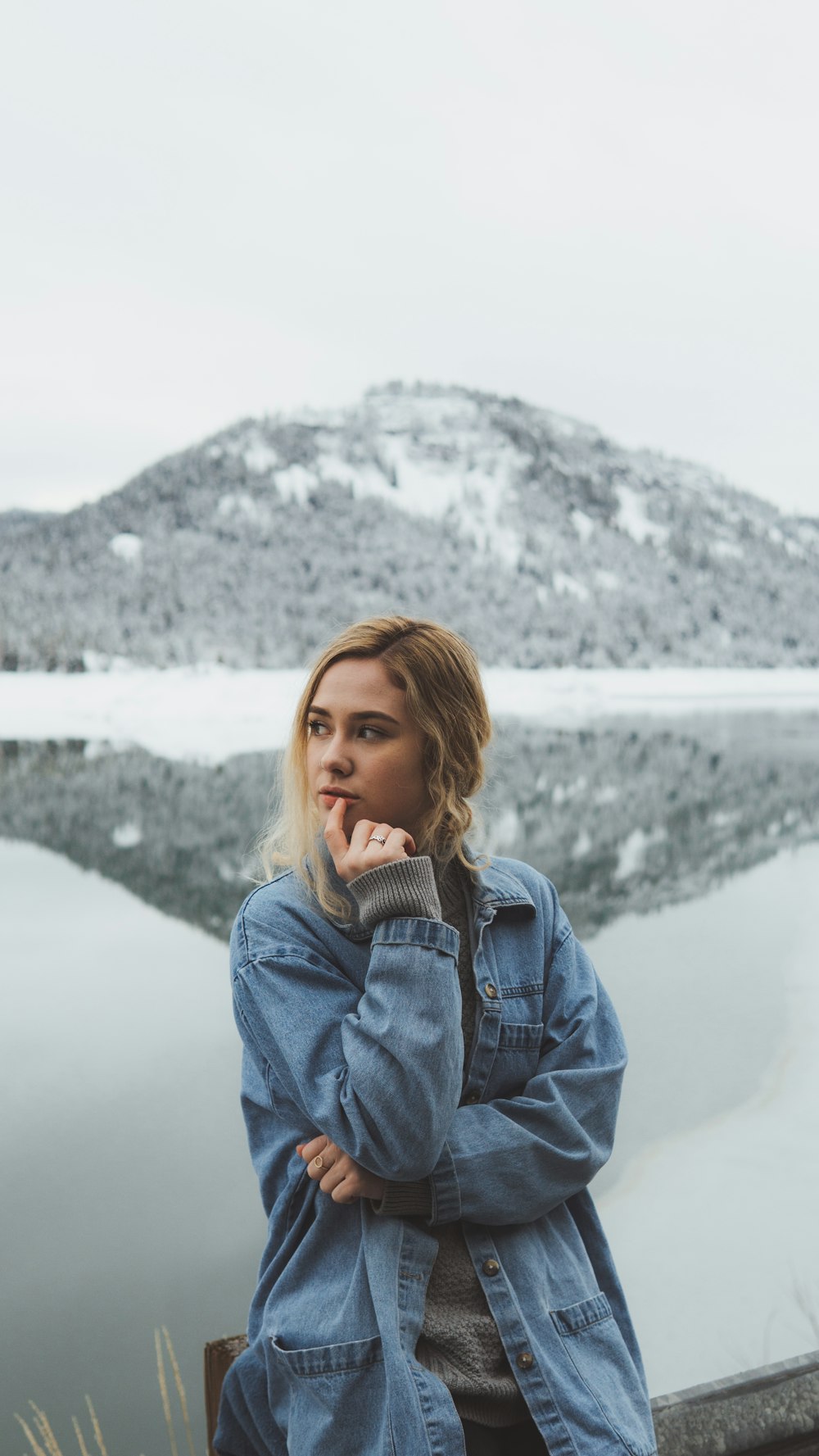 shallow focus photo of woman in blue denim jacket standing near mountain
