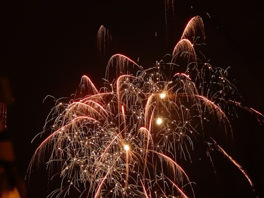 Exploding fireworks light up the night sky with bright trails and sparkles of red and white. The bursts form intricate patterns against the dark backdrop, creating a dazzling visual display.
