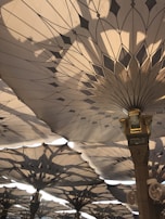 Large architectural umbrellas with intricate geometric patterns provide shade. Sunlight filters through, casting complex shadows on the structures.