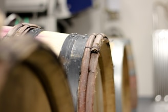 Wooden barrels stacked horizontally in a cellar with metal bands securing the staves. The background is blurred, focusing on the texture and color of the barrels.