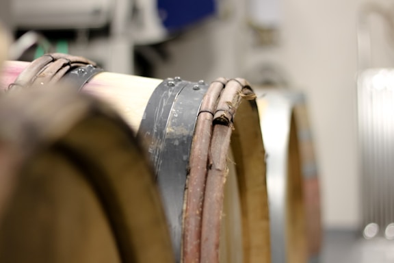 Wooden barrels stacked horizontally in a cellar with metal bands securing the staves. The background is blurred, focusing on the texture and color of the barrels.