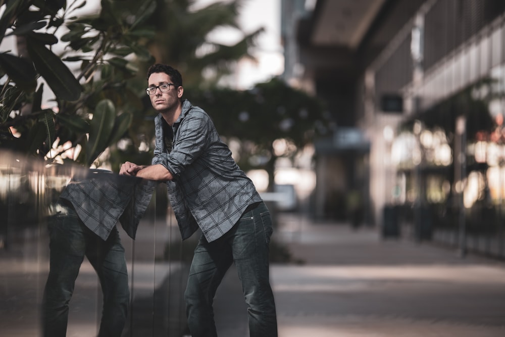 shallow focus photo of man in gray dress shirt leaning on wall