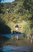 A serene outdoor meditation scene with a person sitting cross-legged on a grassy hill.