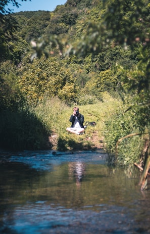 A tranquil outdoor scene with a person seated cross-legged on a mat, surrounded by nature.