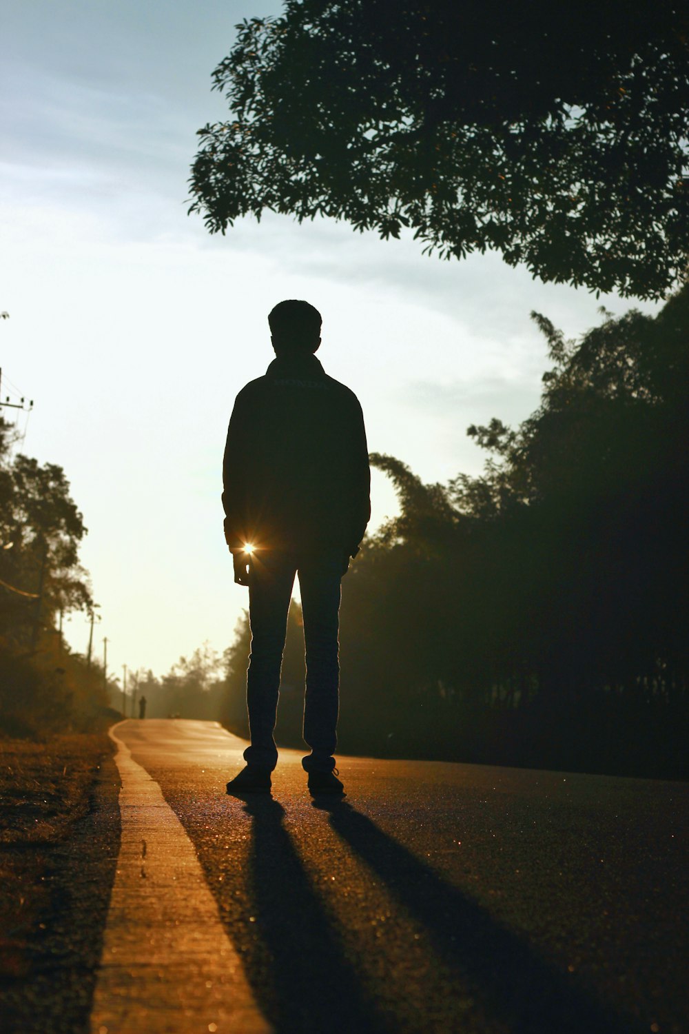 silhouette of man standing on road during sunset