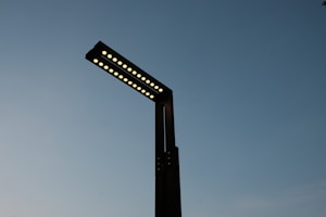 A modern street lamp with multiple LED lights extends into a clear evening sky, displaying a minimalist design with a sleek, dark silhouette.