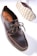 A dark brown leather shoe with detailed stitching and a thick, textured sole is prominently displayed. The shoe features a lace-up design and visible branding on the inner sole. The sole's pattern is visible, showcasing its rugged, slip-resistant design.