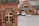 A brick pillar displays a sign for Emmanuel Memorial Episcopal Church. The sign features a decorative cross and shield emblem. In the background, a brick building with a gray roof is visible alongside a parking lot with a few cars.