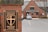 A brick pillar displays a sign for Emmanuel Memorial Episcopal Church. The sign features a decorative cross and shield emblem. In the background, a brick building with a gray roof is visible alongside a parking lot with a few cars.