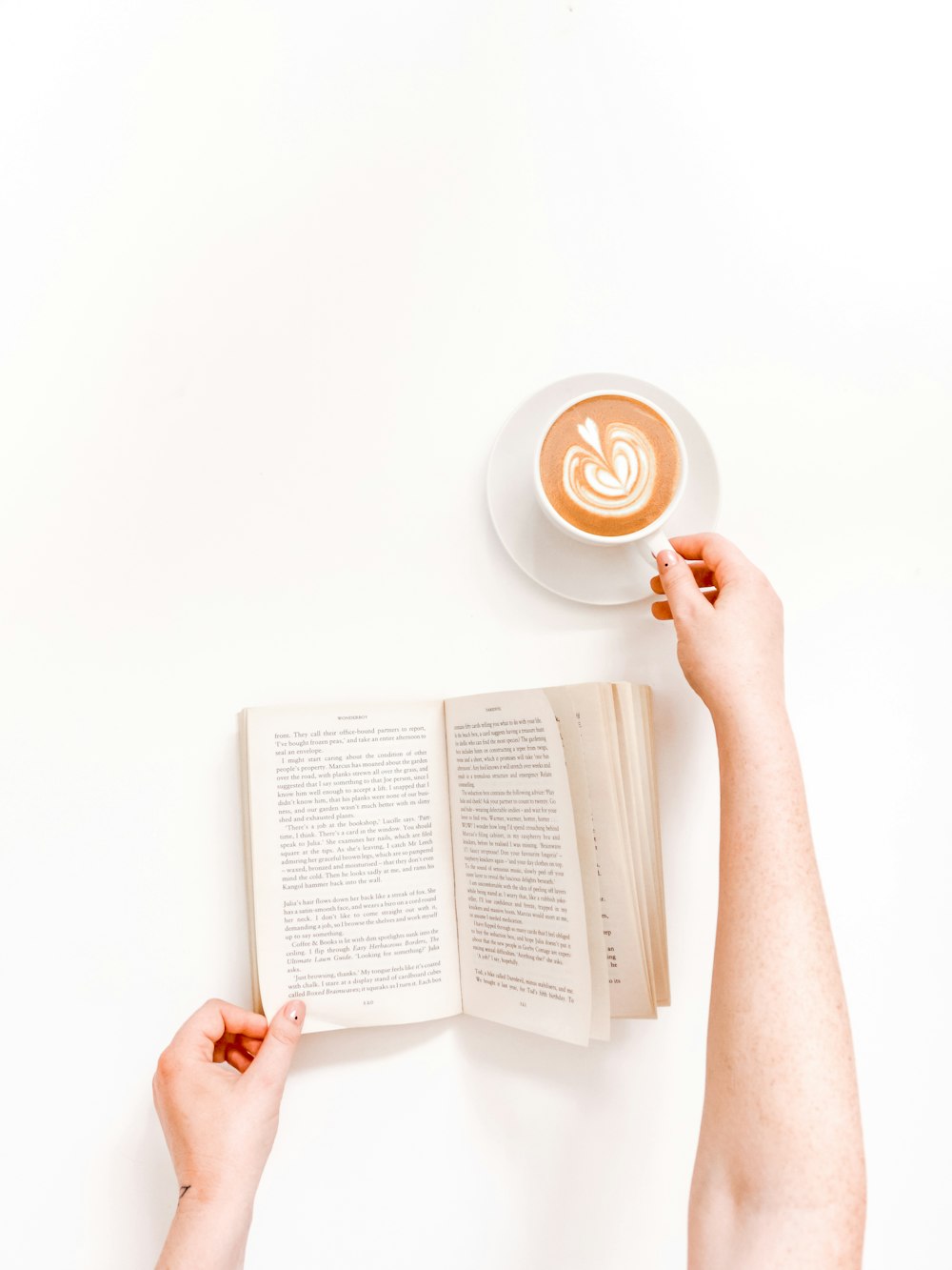 Persona de la fotografía plana que sostiene la taza con el café con leche y el libro
