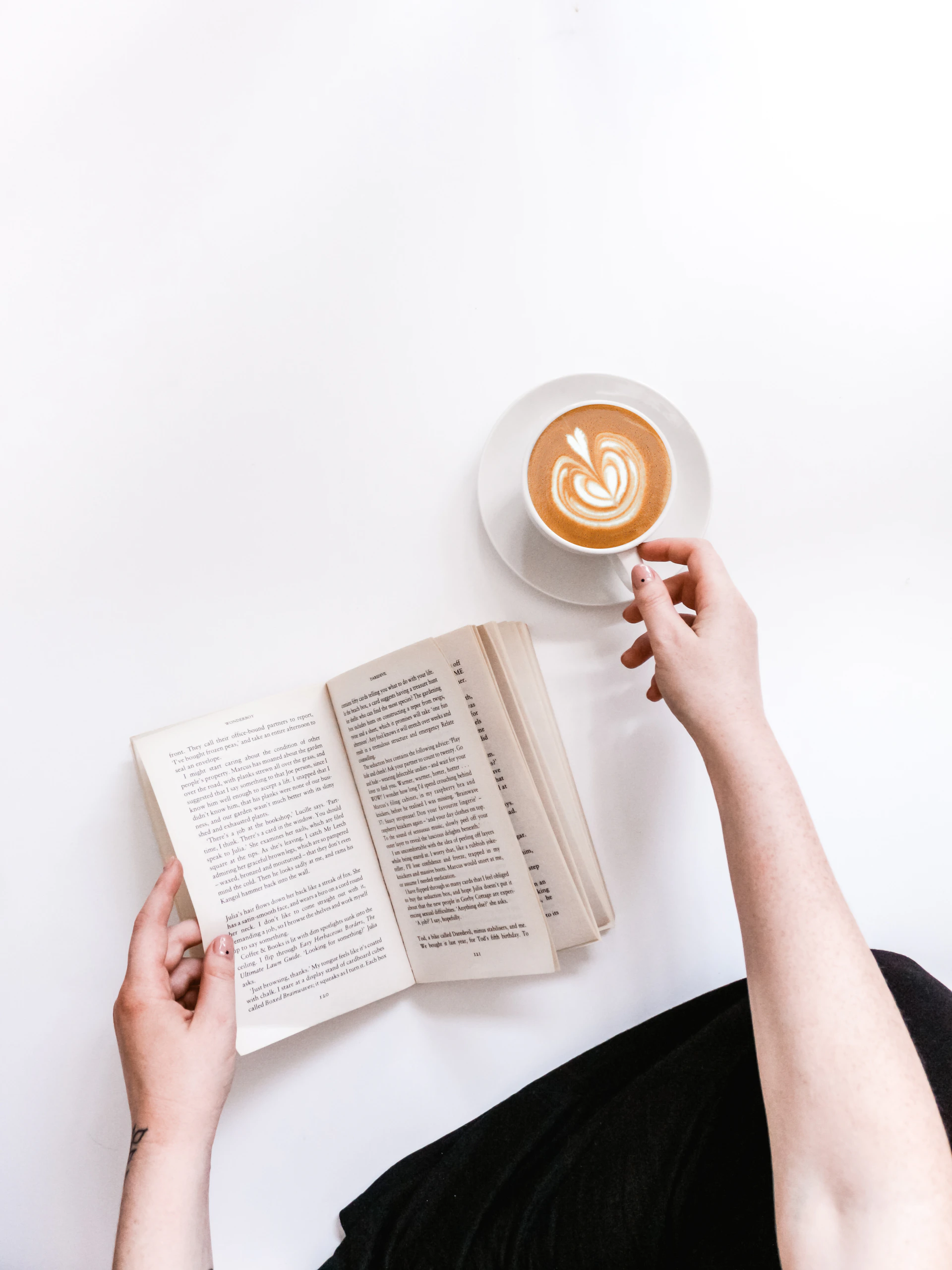 An open book and coffee on a white surface