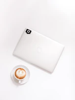 A minimalist setup featuring a pair of headphones beside a laptop and a steaming cup of coffee.