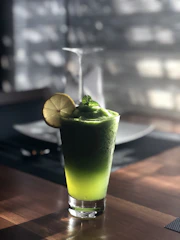 Fresh green smoothie with vibrant fruits on a rustic wooden table, sunlight highlighting natural textures.