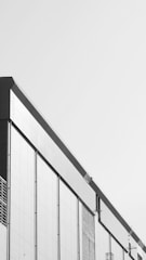 A modern building facade with a minimalist design, featuring clean lines and a monochrome color scheme. The structure has large rectangular panels and subtle architectural details.