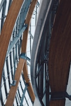 Curved wooden beams and metal architectural elements create a complex and modern structural design. The lines of the materials form an intricate pattern, suggesting a contemporary building or structure with an emphasis on engineering and aesthetics.