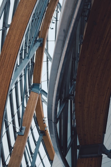 Curved wooden beams and metal architectural elements create a complex and modern structural design. The lines of the materials form an intricate pattern, suggesting a contemporary building or structure with an emphasis on engineering and aesthetics.