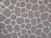 A textured stone wall pattern consisting of variously sized and shaped brown stones arranged in a mosaic with white grout lines between them.